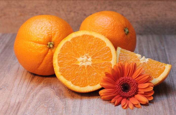 Tri pomaranče, dve sta celi, ena pa narezana na pol, zraven je cvetlica