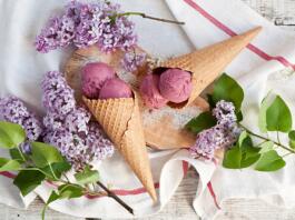 Korneta sladoleda na leseni deski, ki leži na servetu, zraven so vejice rož