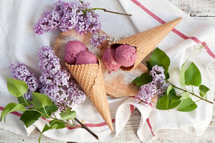 Korneta sladoleda na leseni deski, ki leži na servetu, zraven so vejice rož
