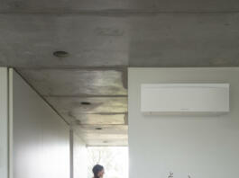 Ženska stoji na hodniku, na steni je klimatska naprava