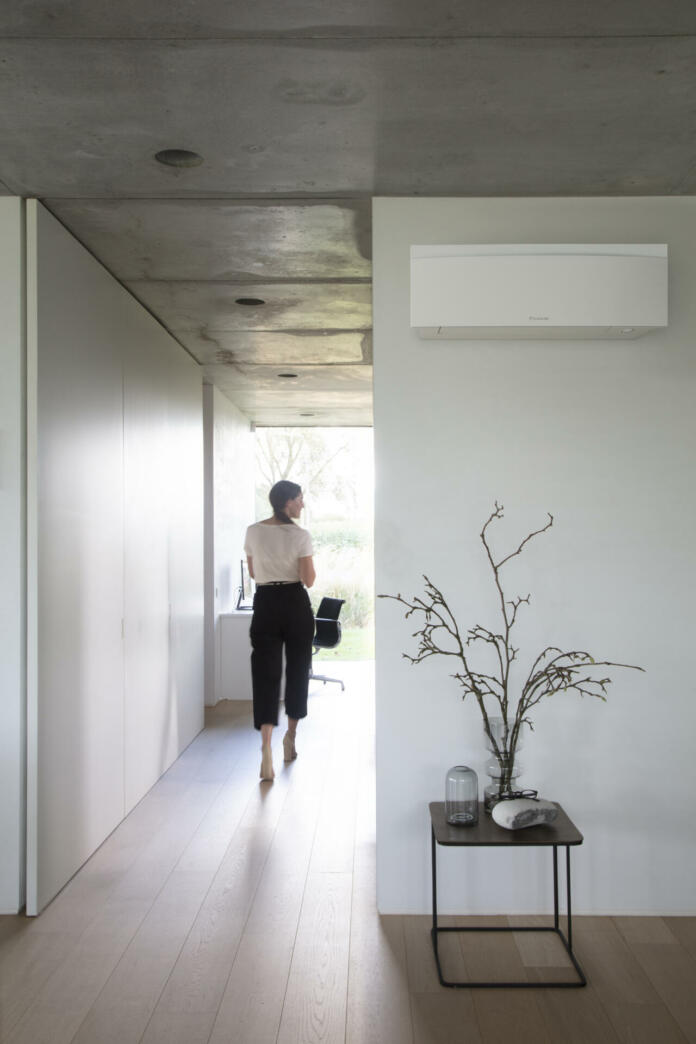 Ženska stoji na hodniku, na steni je klimatska naprava