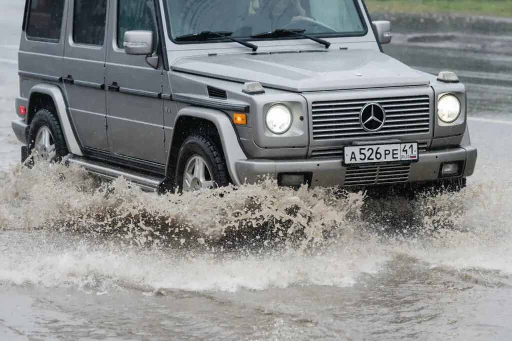 Automobile Mercedes-Benz G-Wagen driving on flooded street road over deep muddy puddle, splashing drop of spray water from wheels. Petropavlovsk-Kamchatsky, Kamchatka Peninsula, Russia - Aug 18, 2018