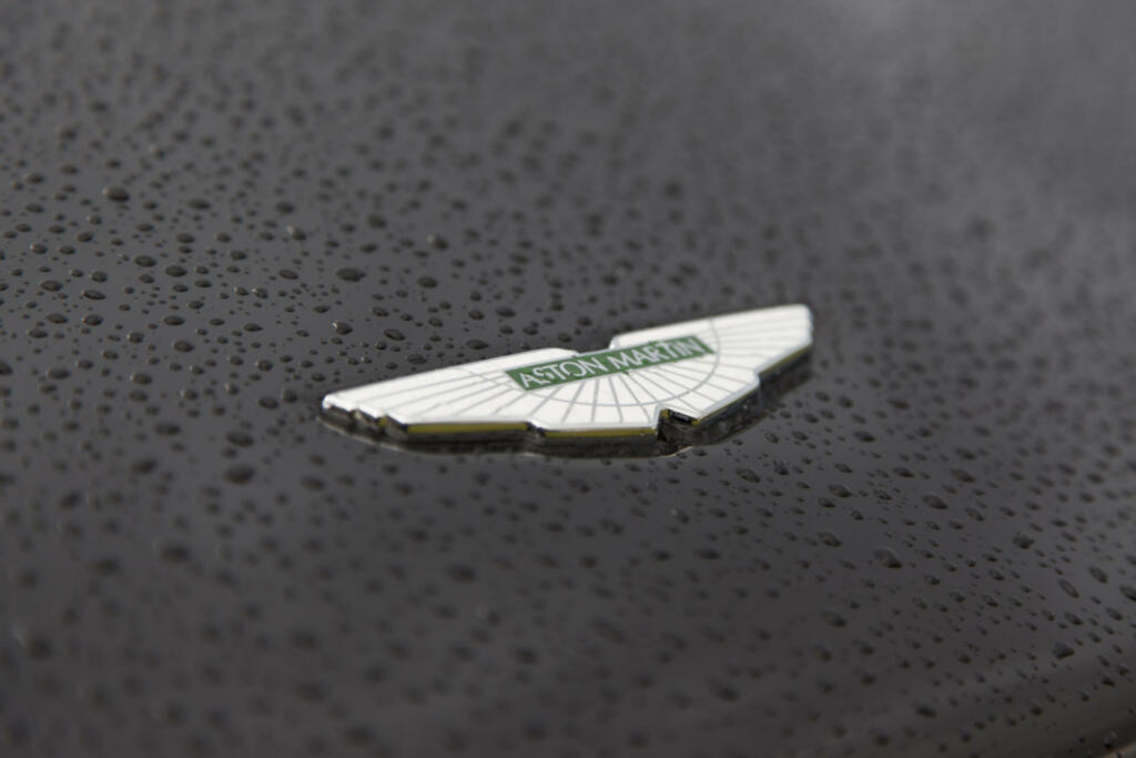 Newport Pagnell, United Kingdom - October 15, 2012: An Aston Martin sports car bonnet with wet brand logo. Aston Martin is a British Car Manufacturer founded in 1913 by Lionel Martin and Robert Bamford as Bamford and Martin Ltd. They changed the name 1914 in Aston Martin. They produce luxury sportscar. This Aston Martin is parking in front of an Aston Martin Dealership.