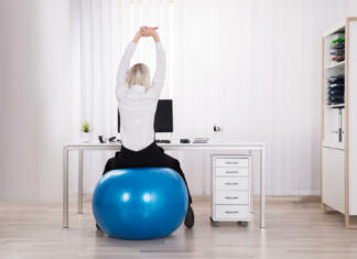 Prednosti pilates žoge pri našem zdravju Rear View Of Businesswoman Sitting On Fitness Ball Stretching Her Arms In Office