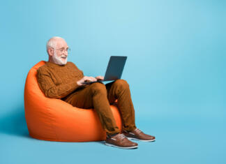 Izobraževanja za odrasle se morajo ustaviti: Kaj to pomeni za digitalni bon? Portrait of his he nice, attractive focused bearded grey-haired man sitting in bag chair using laptop writing email letter browsing web wi-fi isolated over blue pastel color background