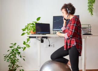 Nastavljiva miza: rešitev za domačo pisarno ali otroško sobo Woman teleworking at an adjustable standing desk with one knee resting on a fitball