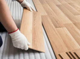 Installing laminated floor, detail on man hands with white gloves fitting wooden tile, over white foam base layer.