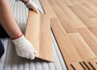 Prednosti in slabosti laminata Installing laminated floor, detail on man hands with white gloves fitting wooden tile, over white foam base layer.