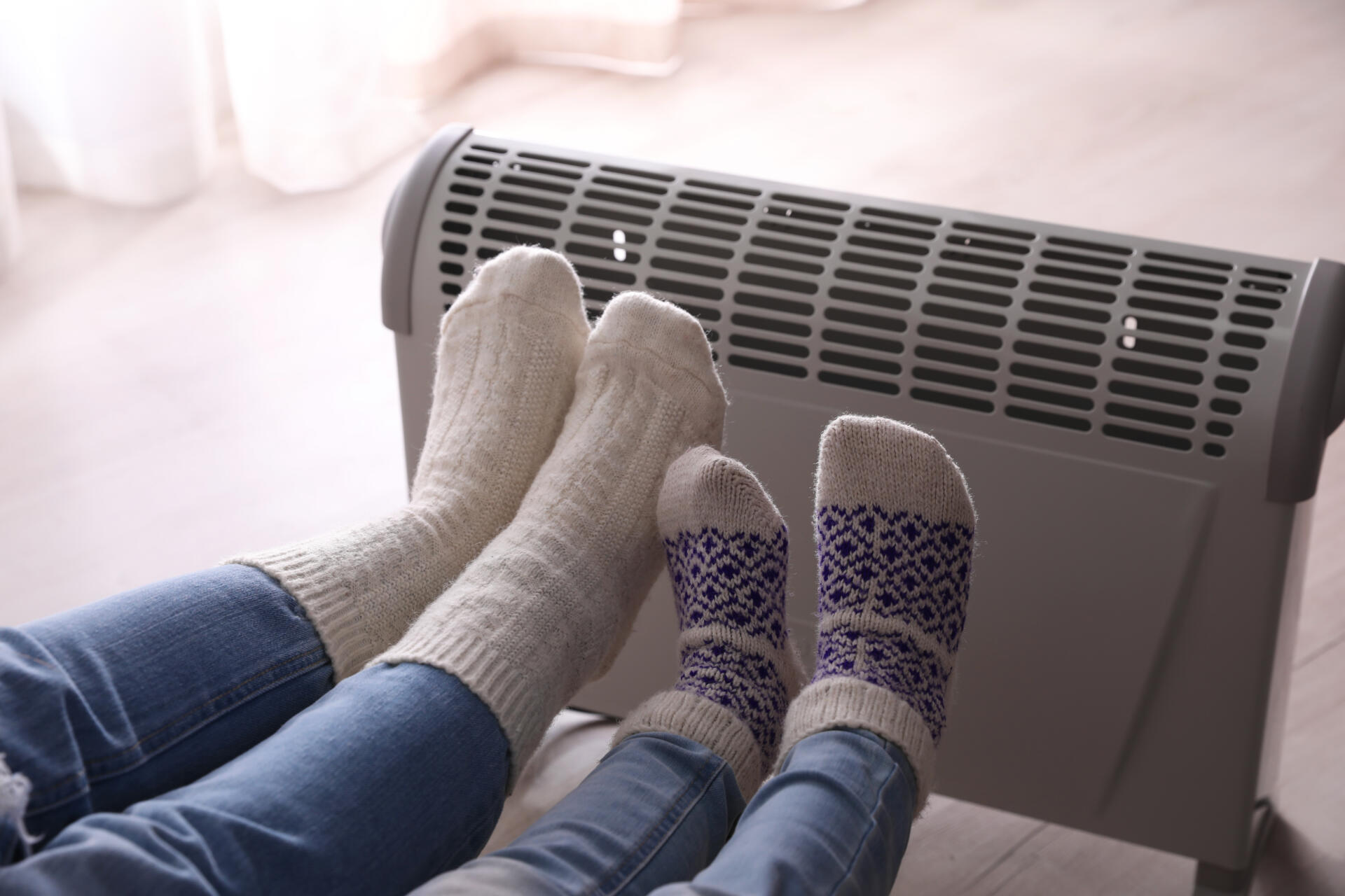 Mother and child warming feet near electric heater at home, closeup