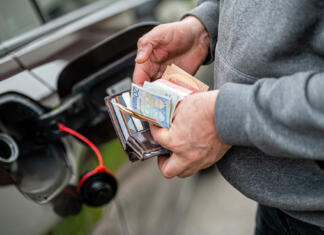 86 milijonov evrov pomoči gospodarstvu zaradi draginje a man s hand counts money while standing at an open fuel tank, the concept of rising fuel prices