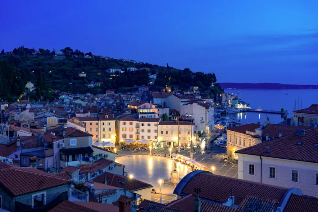 Beautiful sunset in Piran with Tartini square at night with city lights .