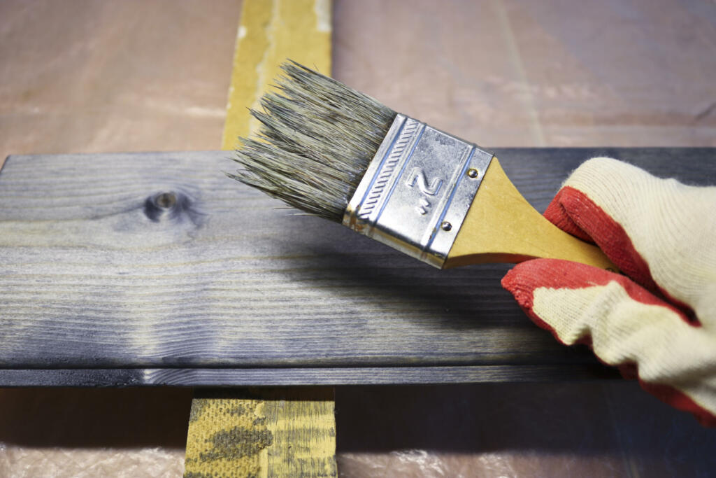 Handling a woody pine plank with a dark mordant with a paintbrush for deeply impregnating wood for painting purposes. Carpentry and painting works.