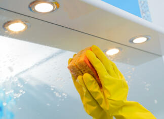 Kako enostavno očistiti ogledala A woman polishing glass using a cleaning sponge and rubber gloves cleaning a mirror with a spray cleaner