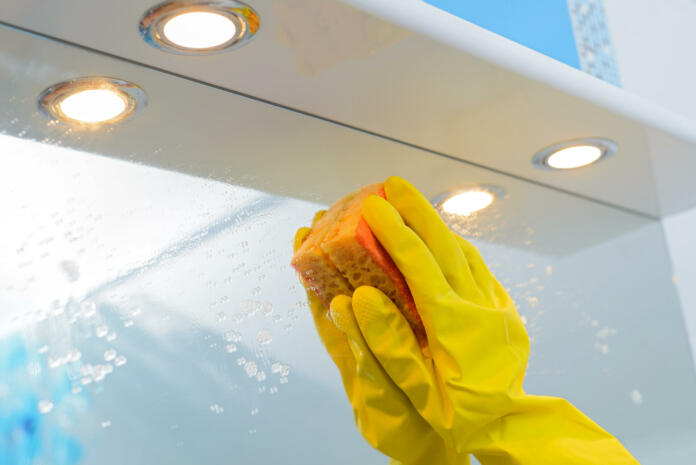 A woman polishing glass using a cleaning sponge and rubber gloves cleaning a mirror with a spray cleaner