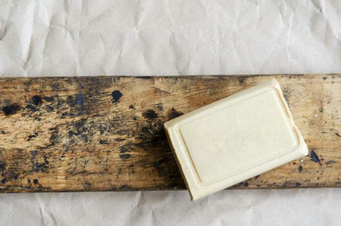 Briquette of laundry soap on an old wooden board. Demonstration of a single piece of new soap. Place for text. Natural hygiene products. Selective focus.