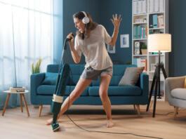 Cheerful woman cleaning up her home and singing, she is using the vacuum cleaner as a microphone