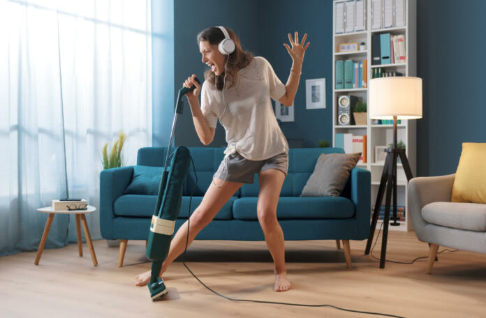 Cheerful woman cleaning up her home and singing, she is using the vacuum cleaner as a microphone