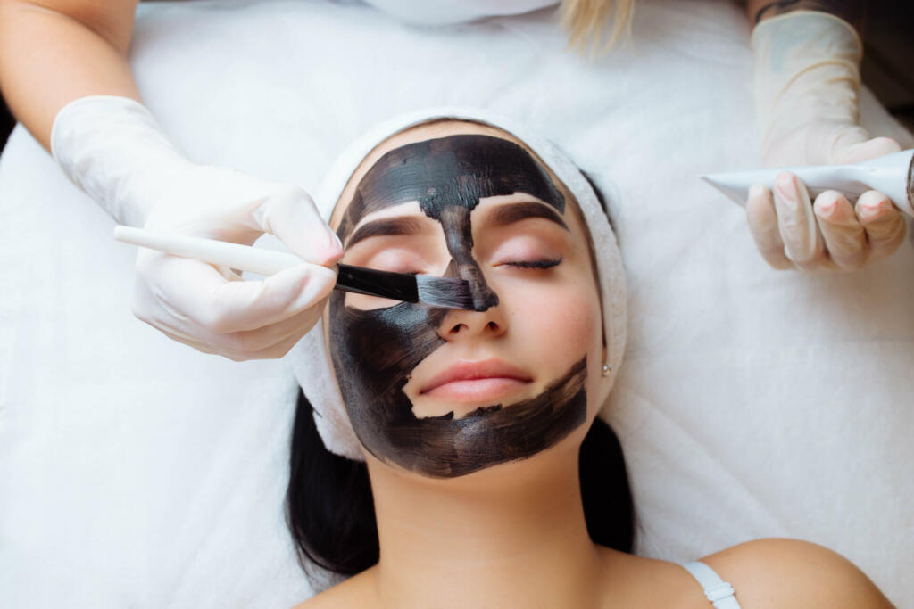 Kozmetičarka nanaša črno masko na obraz ženske