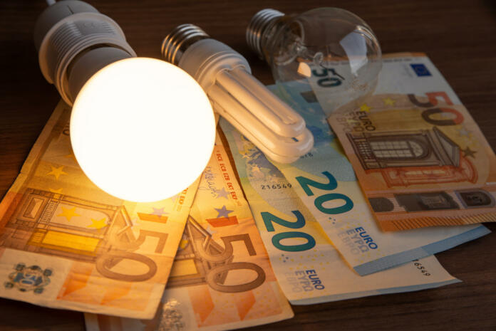 LED bulb on, with fluorescent bulb and incandescent bulb, with bills and coins next to it. Energy costs and evolution of light bulbs.