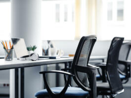 Modern gadgets in interior of coworking office during COVID-19 epidemic. Chairs and desk for support workers, laptops and headphones, cups and stationery in daylight on window background, free space