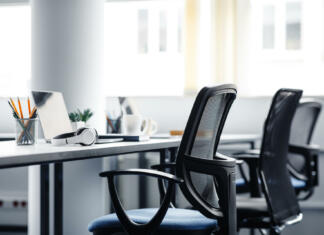 To morate vedeti o izbiri pisarniškega stola Modern gadgets in interior of coworking office during COVID-19 epidemic. Chairs and desk for support workers, laptops and headphones, cups and stationery in daylight on window background, free space