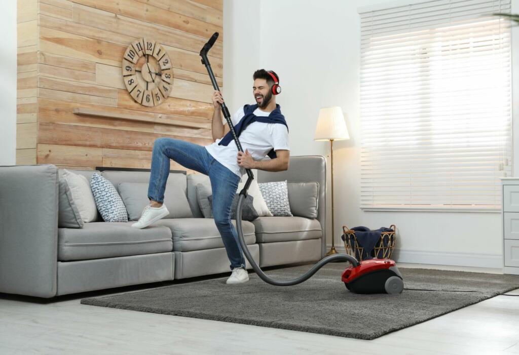 Young man having fun while vacuuming at home