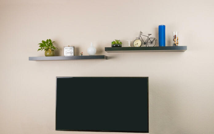 Black wall mounted and decorated shelves and wall mounted television unit are mounted and displayed on the wall.