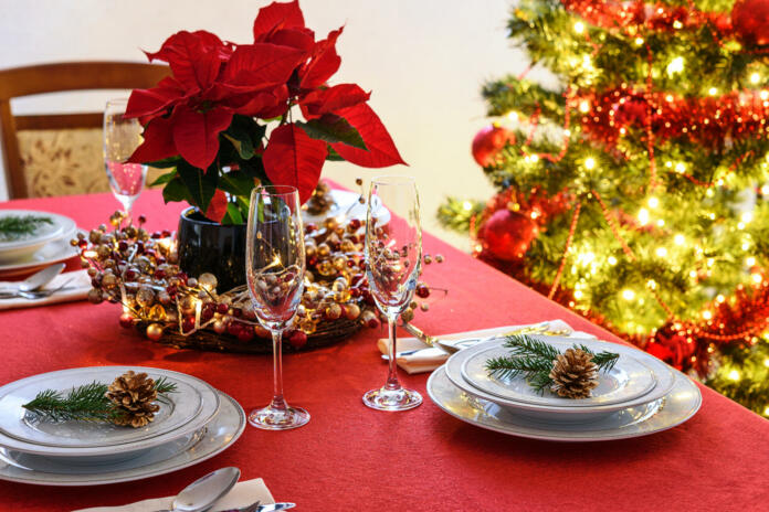 Christmas table decoration concept - champagne glasses, red poinsettia and table setting on a background of colorful Christmas decoration.
