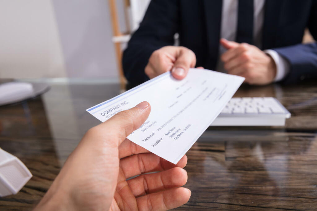 Close-up Of A Businessperson's Hand Giving Cheque To Colleague At Workplace