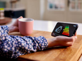 Close Up Of Woman Holding Smart Energy Meter In Kitchen Measuring Energy Efficiency