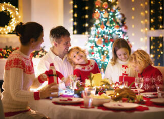 10 korakov do popolnega božičnega večera Family with children eating turkey Christmas dinner at fireplace and decorated Xmas tree. Parents, grandparents and kids at festive meal. Winter holidays celebration and food. Kids open presents.