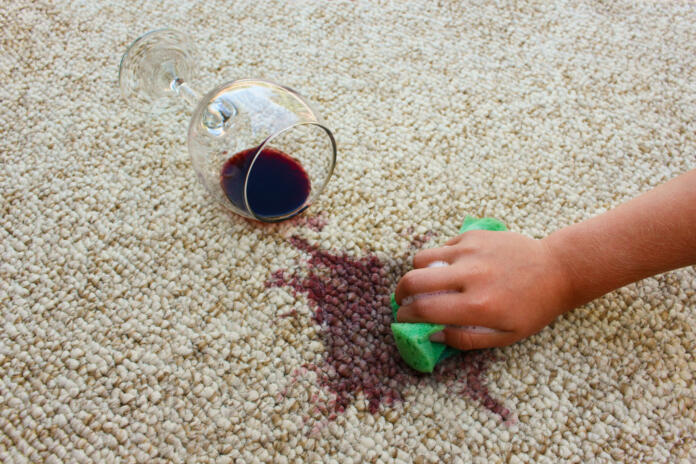 Glass of red wine fell on carpet. Female hand cleans floor with sponge and detergent.