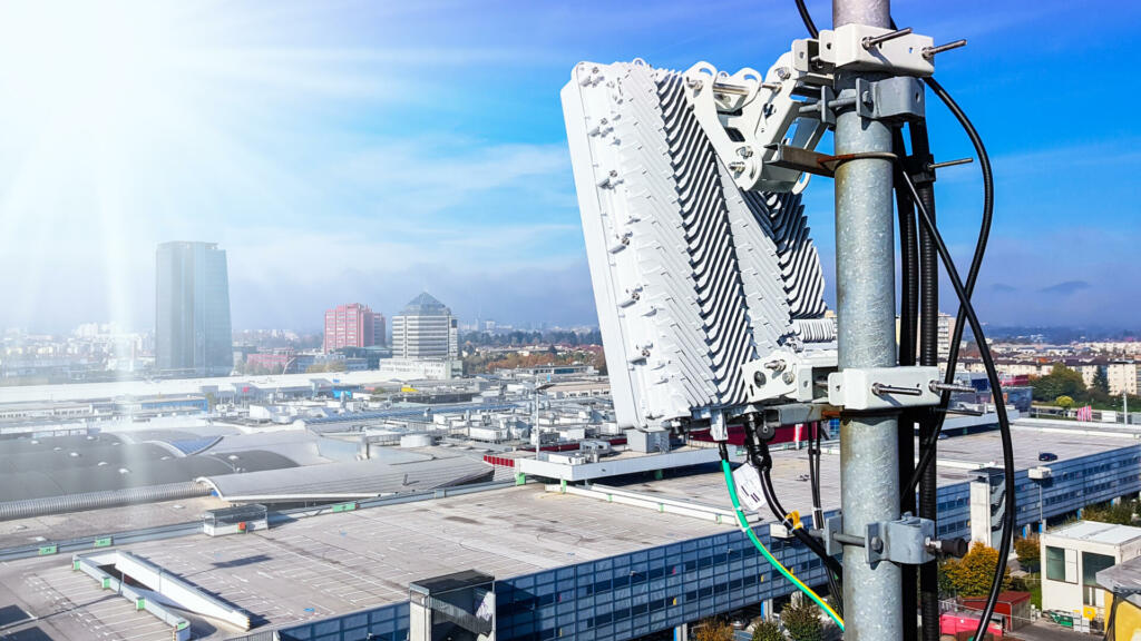 Mobile telecommunication cellular radio network antennas on a mast on the roof broadcasting signal waves over the city on a clear sunny day with blue sky and clouds