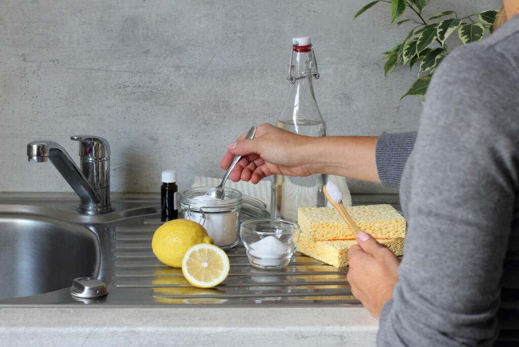 Vinegar, bicarbonate of soda, lemon, sponge, bamboo toothbrush, cotton towels on the kitchen stainless stil sink next to the tap.