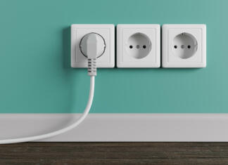 A white electrical outlet on the wall in the room. An electric plug with a cable in the socket.