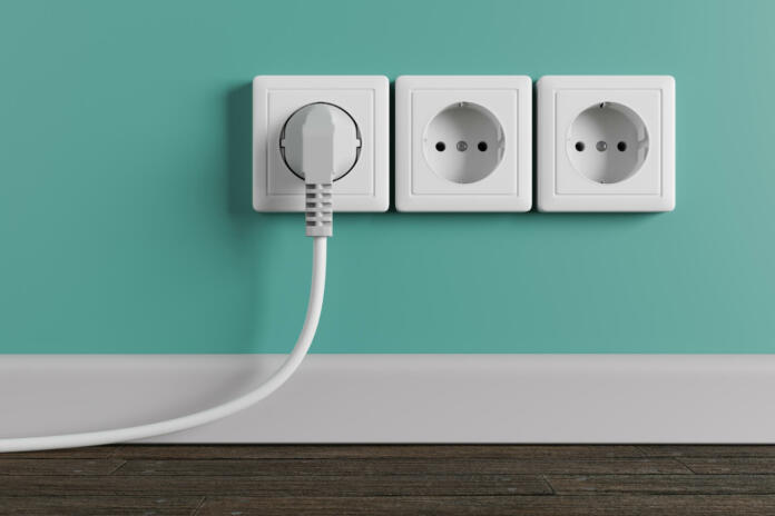 A white electrical outlet on the wall in the room. An electric plug with a cable in the socket.