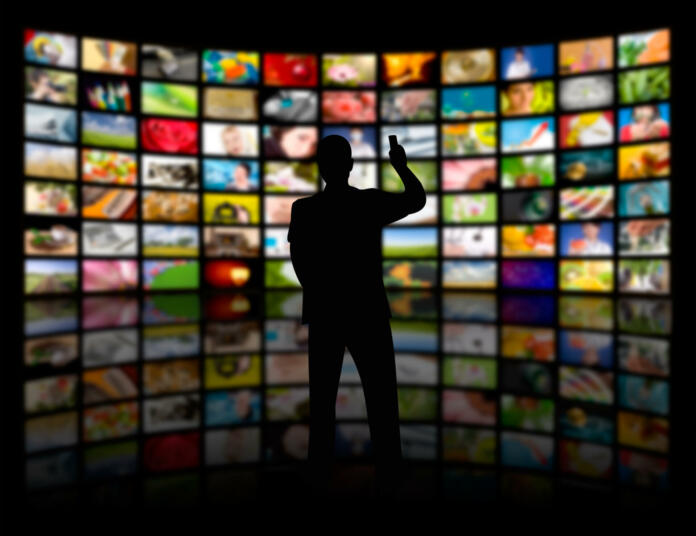 Back view of a young man watching a big TV panel