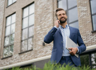 Iščemo tržnika oglasnih kapacitet spletnih in tiskanih medijev (M/Ž) Handsome smiling businessman wearing stylish suit talking on mobile phone, holding laptop standing on the street. Successful business