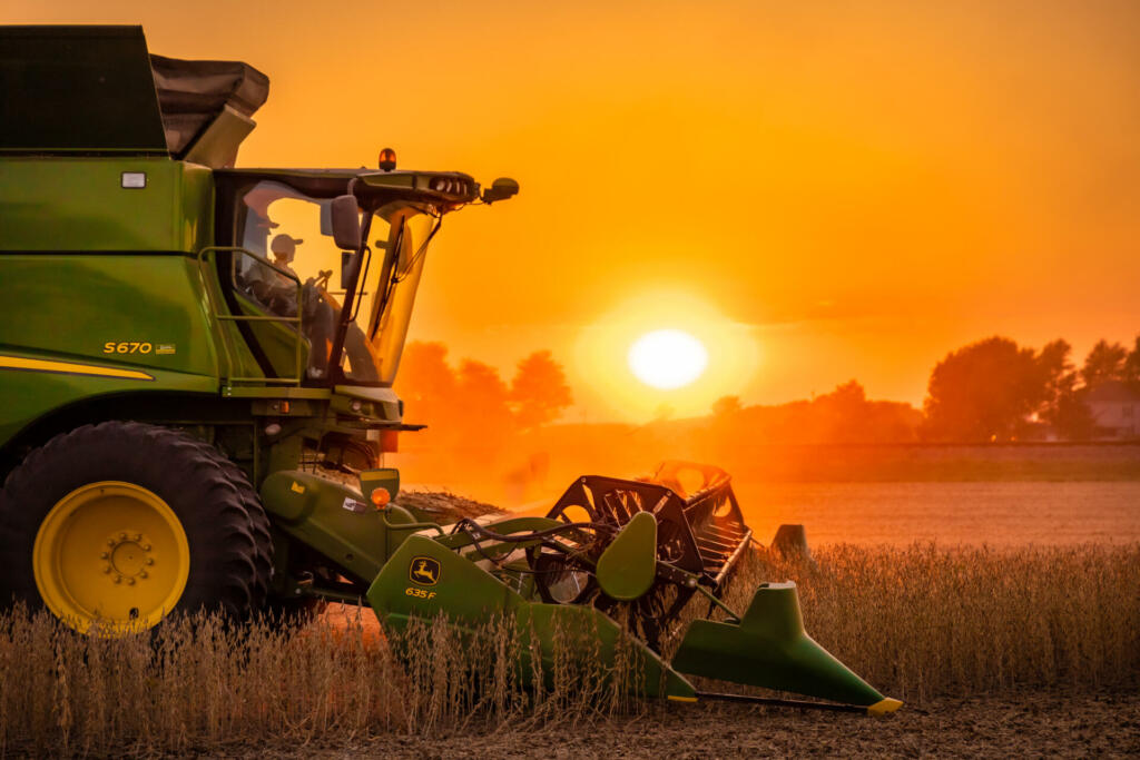 Henry County, Ohio - September 25, 2020: A profile view of a John Deere S670 harvesting soybeans during a hazy sunset with a red and orange sky from the bean dust.
