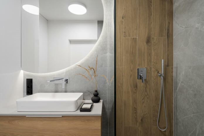 Modern bathroom with wooden style tiles in shower cabin next to big, round mirror with led light above washbasin