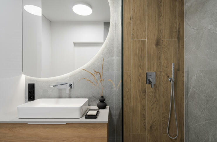 Modern bathroom with wooden style tiles in shower cabin next to big, round mirror with led light above washbasin