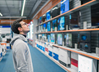 Vodič po nakupu televizorjev (del 1): vrste televizorjev Smart modern male customer choosing large TV-sets at electronics store. He looks wondered. New screen generations.