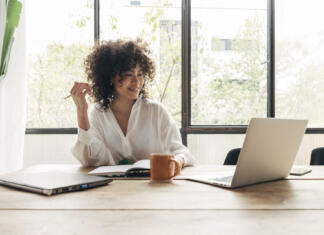 Zaposlimo pisca: MojPrihranek išče novinarja (M/Ž) Smiling, happy, Young beautiful african american woman studying at home with laptop. Taking notes in notebook. Bright spacious living room. E-learning concept. Study at home concept.