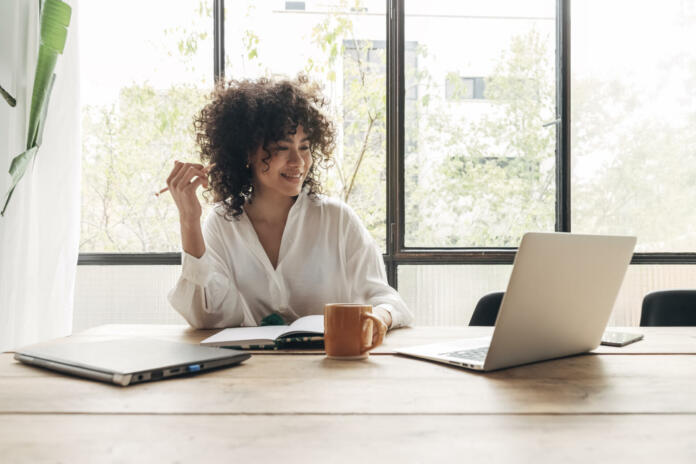 Smiling, happy, Young beautiful african american woman studying at home with laptop. Taking notes in notebook. Bright spacious living room. E-learning concept. Study at home concept.