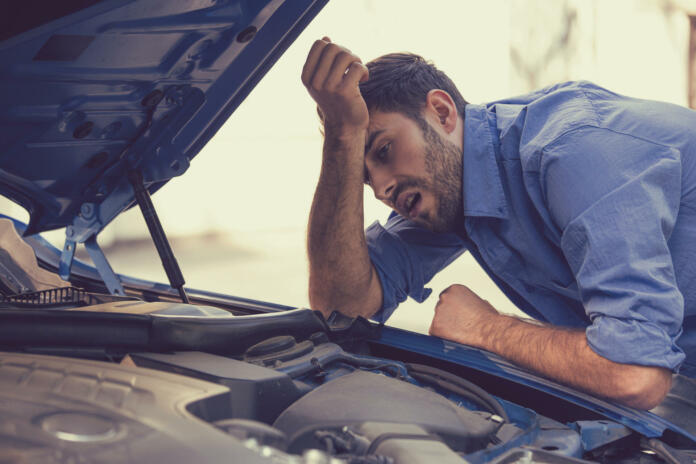young stressed man having trouble with his broken car looking in frustration at failed engine