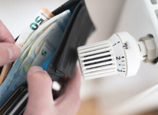 Kako vzdrževati radiatorje med kurilno sezono in kako zmanjšati stroške ogrevanja close-up view of person holding wallet with cash next to turned down thermostat on radiator, rising energy and heating costs concept