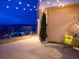 cozy rooftop terrace with rattan hanging chair, garlands and beautiful landscape at night