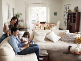 Young Hispanic family sitting on sofa reading a book together in their living room