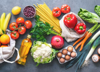 5 priljubljenih diet in njihov ekološki vpliv Groceries shopping. Flat lay of fruits, vegetables, greens, bread and oil in eco friendly bags, top view. Healthy eating and sustainability concept