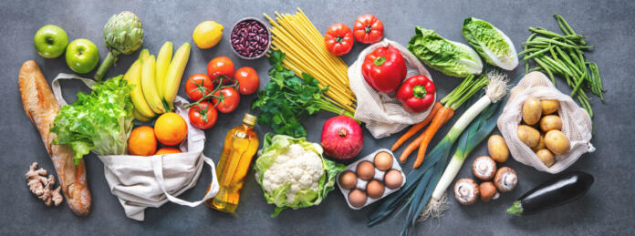 Groceries shopping. Flat lay of fruits, vegetables, greens, bread and oil in eco friendly bags, top view. Healthy eating and sustainability concept